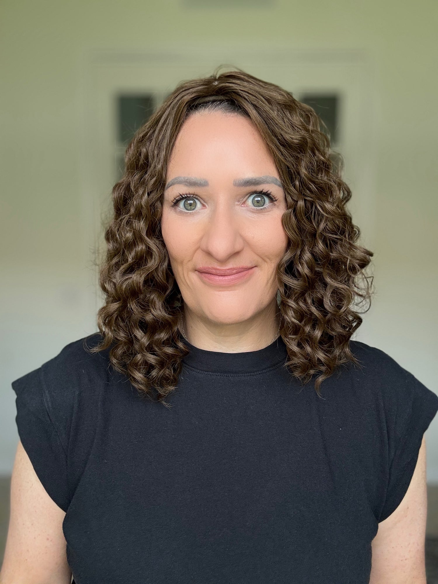 Woman with curly hair topper wearing a black shirt against a neutral background