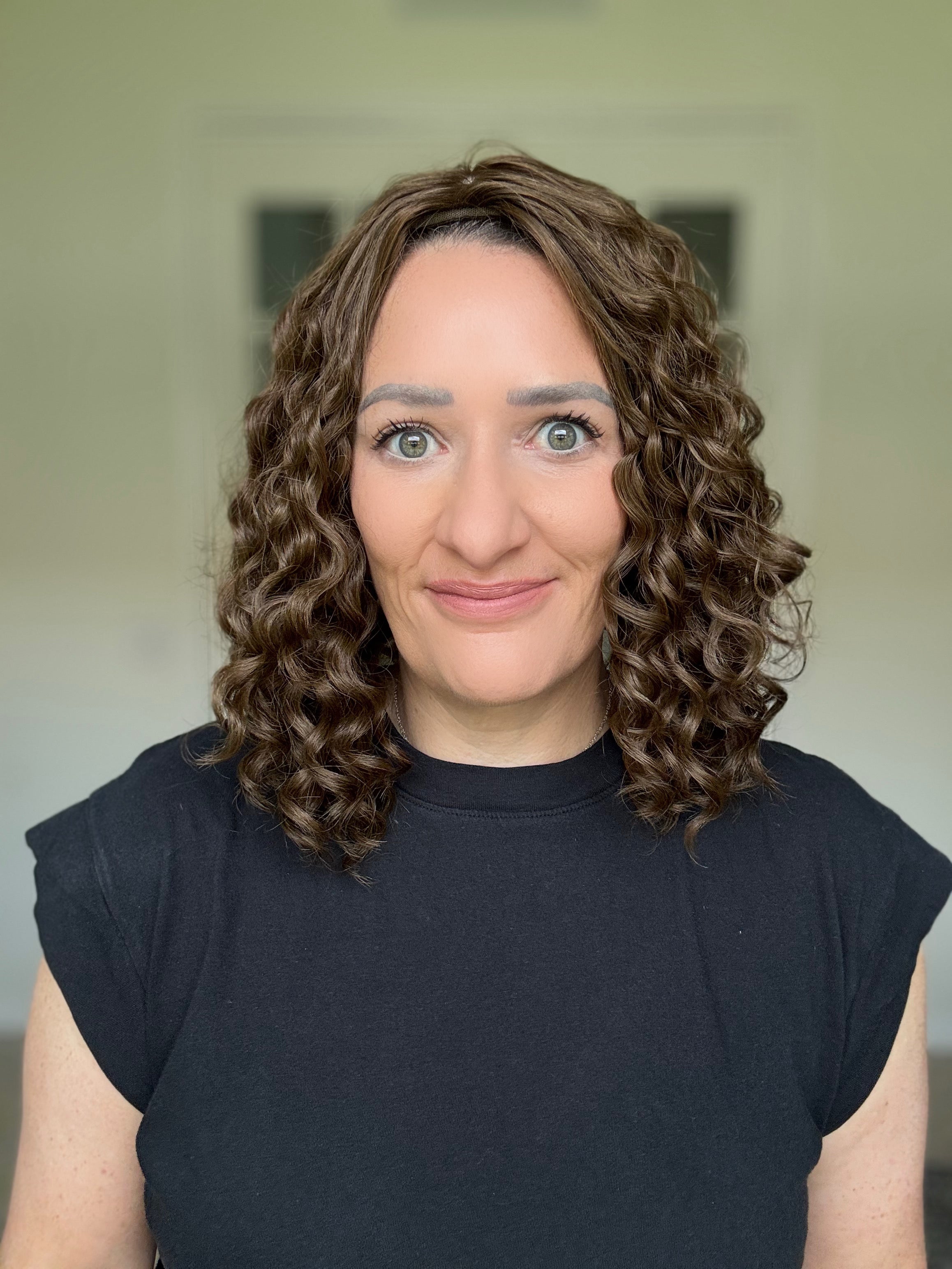 Woman with curly hair topper wearing a black shirt against a neutral background